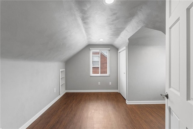 additional living space featuring vaulted ceiling, a textured ceiling, baseboards, and wood finished floors