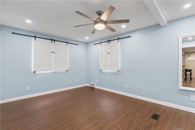 empty room with dark wood-style floors, a barn door, baseboards, and a ceiling fan