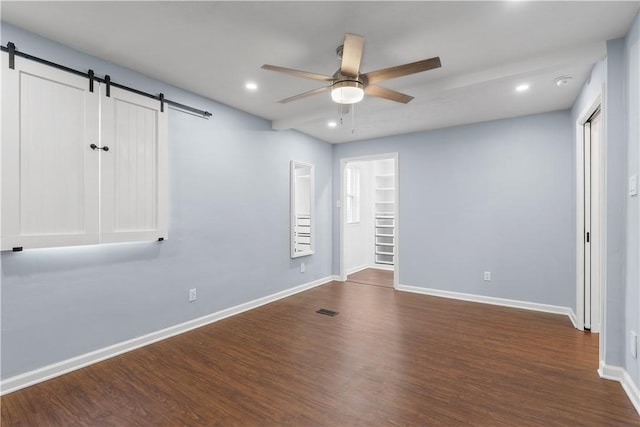 spare room with dark wood-style floors, recessed lighting, a barn door, a ceiling fan, and baseboards