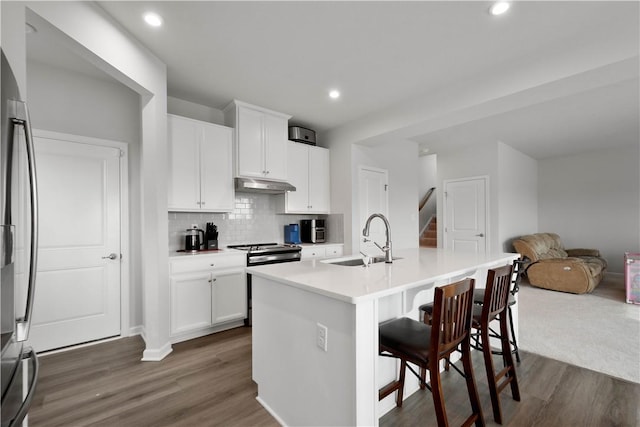 kitchen featuring dark wood finished floors, a breakfast bar, refrigerator, under cabinet range hood, and a sink