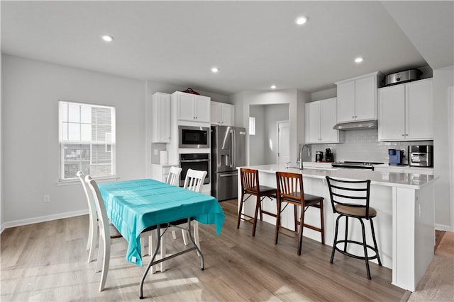 kitchen with a center island with sink, decorative backsplash, appliances with stainless steel finishes, under cabinet range hood, and a kitchen bar