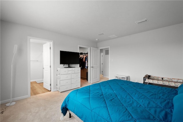 bedroom with ensuite bathroom, light carpet, visible vents, baseboards, and a spacious closet