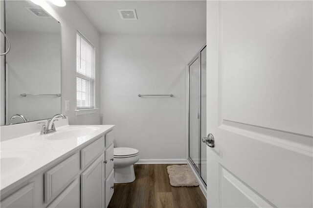 bathroom featuring double vanity, visible vents, wood finished floors, a shower stall, and a sink