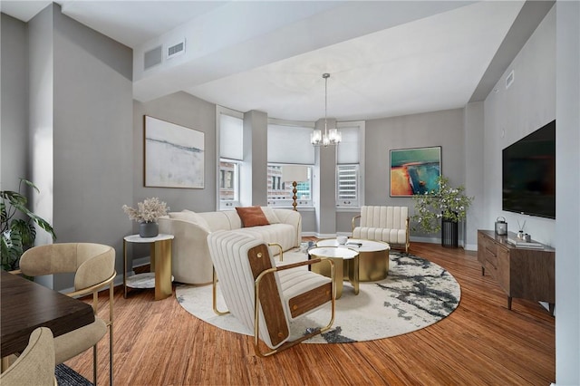 living room with an inviting chandelier, baseboards, visible vents, and wood finished floors