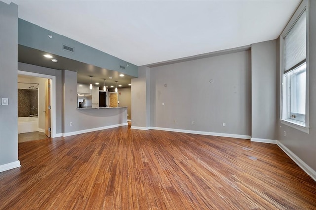 unfurnished living room featuring wood finished floors, visible vents, and baseboards