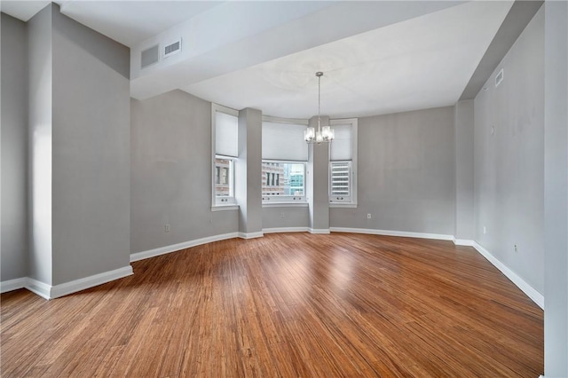 empty room with a chandelier, wood finished floors, visible vents, and baseboards