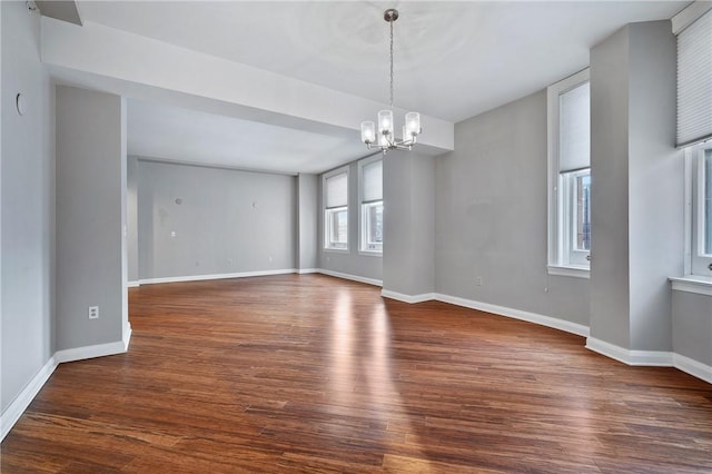 empty room featuring a chandelier, baseboards, and wood finished floors