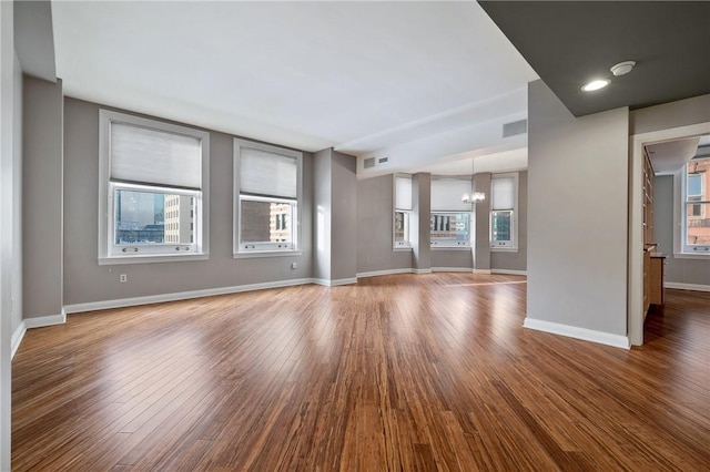 unfurnished living room featuring visible vents, a notable chandelier, baseboards, and wood finished floors