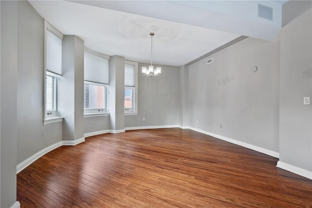 spare room featuring hardwood / wood-style flooring, baseboards, visible vents, and an inviting chandelier