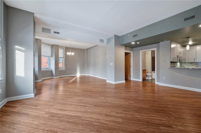 unfurnished living room with baseboards, visible vents, a chandelier, and wood finished floors