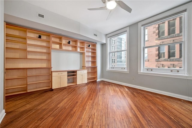 unfurnished living room featuring visible vents, built in desk, baseboards, and wood finished floors