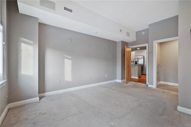 unfurnished room with carpet, visible vents, and baseboards