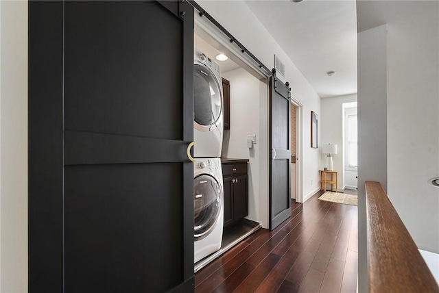 laundry room featuring stacked washer and dryer, a barn door, visible vents, dark wood finished floors, and baseboards