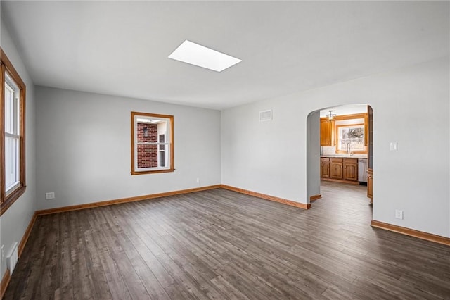 empty room featuring visible vents, arched walkways, baseboards, and dark wood-style floors