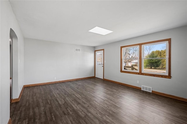 empty room with a skylight, baseboards, visible vents, and dark wood-style flooring