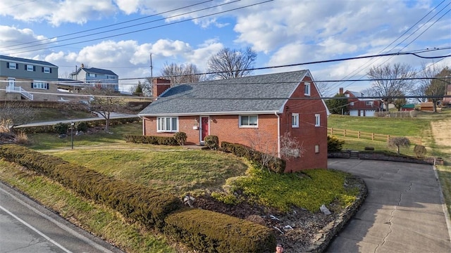 view of front of home with brick siding, roof with shingles, a chimney, fence, and a front lawn