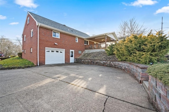 view of side of property featuring a garage, concrete driveway, a ceiling fan, and brick siding