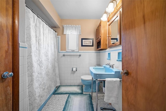 bathroom featuring curtained shower, wainscoting, tile walls, and toilet