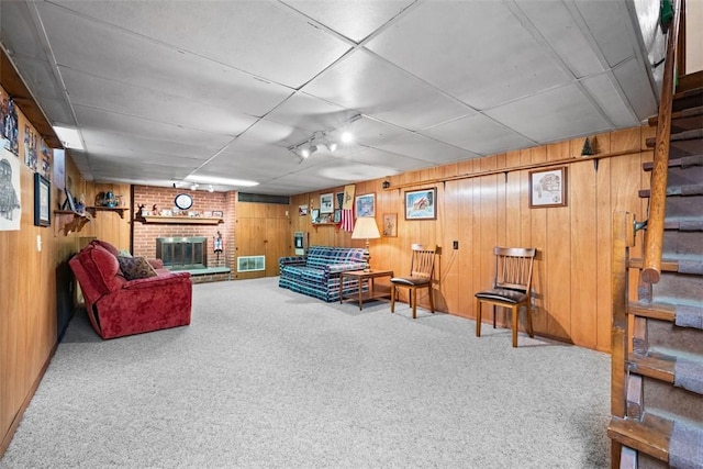 carpeted living room with stairs, wood walls, a brick fireplace, and visible vents