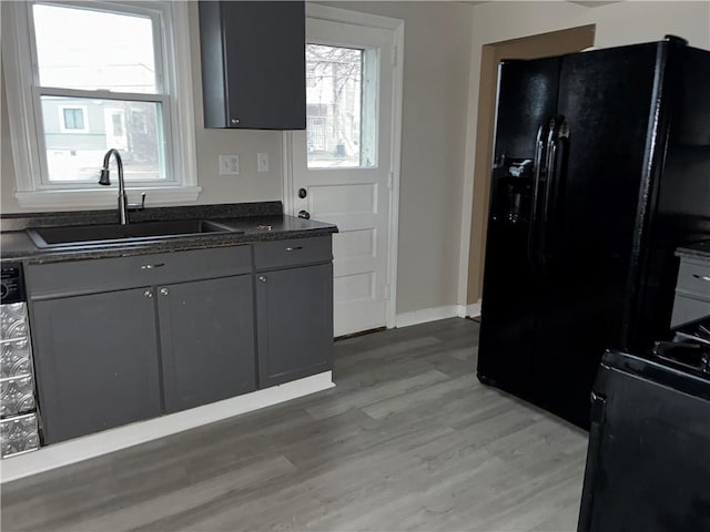 kitchen with light wood finished floors, baseboards, black refrigerator with ice dispenser, gray cabinetry, and a sink