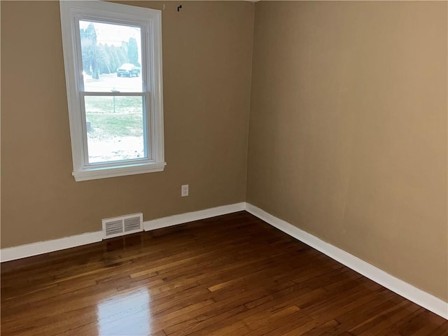 unfurnished room with visible vents, dark wood finished floors, and baseboards