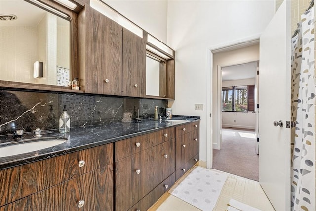 kitchen featuring baseboards, dark stone countertops, a sink, carpet floors, and backsplash