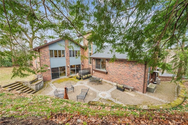 rear view of property with brick siding, roof with shingles, and a patio area