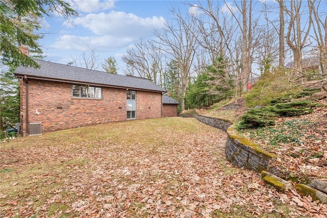 rear view of property featuring central air condition unit, brick siding, roof with shingles, a lawn, and a chimney