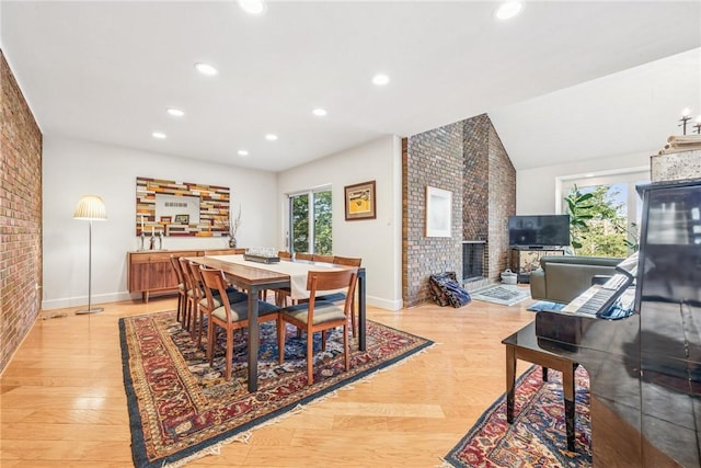 dining area with brick wall, vaulted ceiling, light wood-type flooring, a fireplace, and recessed lighting