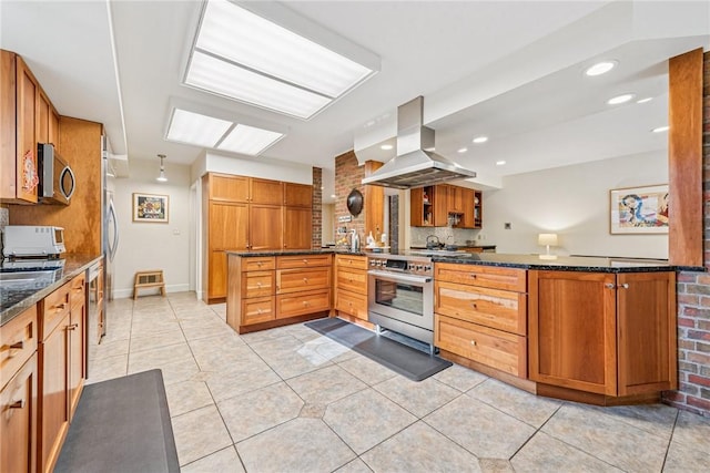 kitchen featuring light tile patterned floors, dark stone countertops, a peninsula, island exhaust hood, and stainless steel appliances