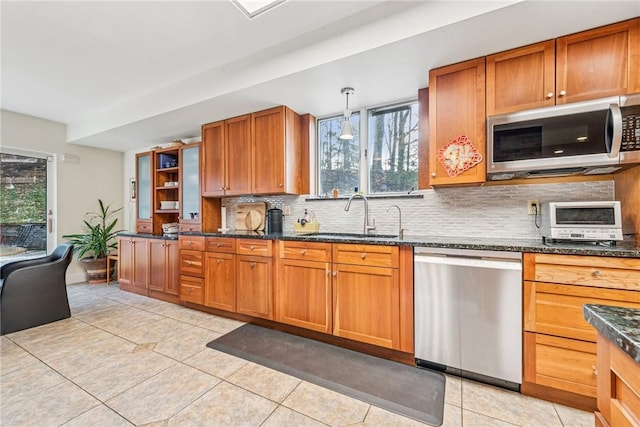 kitchen featuring light tile patterned floors, stainless steel appliances, tasteful backsplash, brown cabinetry, and a sink