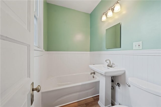 full bath with toilet, a wainscoted wall, a sink, wood finished floors, and a bath