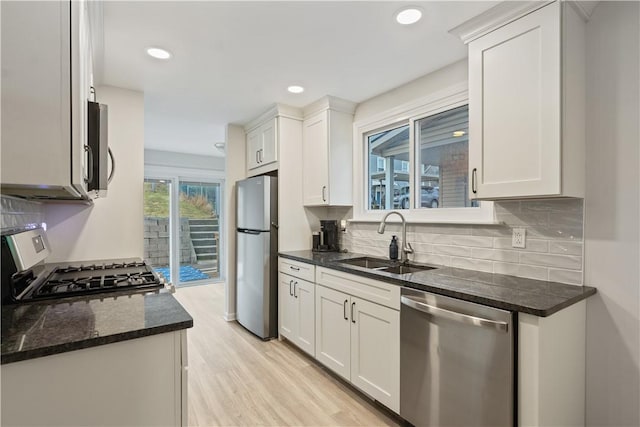 kitchen featuring appliances with stainless steel finishes, light wood-style floors, white cabinetry, a sink, and dark stone counters