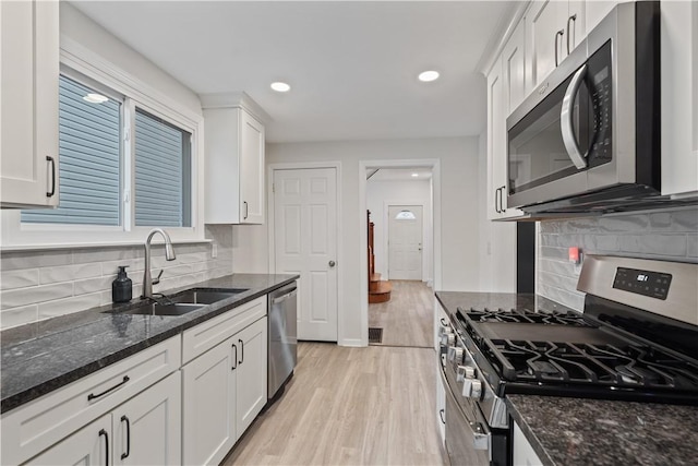 kitchen featuring dark stone counters, stainless steel appliances, a sink, and white cabinetry