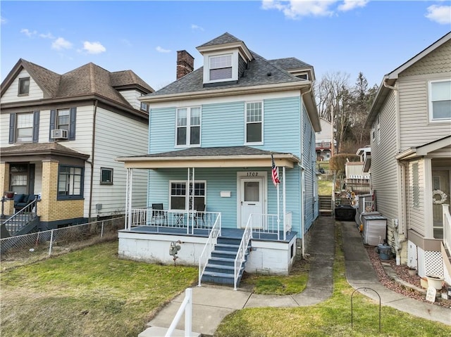 american foursquare style home with covered porch, fence, roof with shingles, a chimney, and a front yard