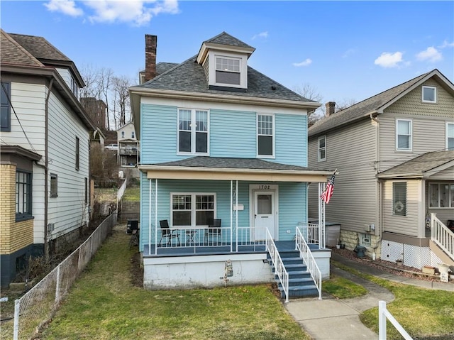 traditional style home featuring a chimney, a porch, a shingled roof, a front yard, and fence