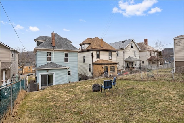 rear view of property with an outdoor fire pit, a lawn, and a fenced backyard