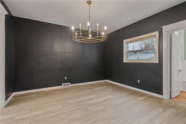 empty room featuring visible vents, baseboards, a chandelier, and wood finished floors