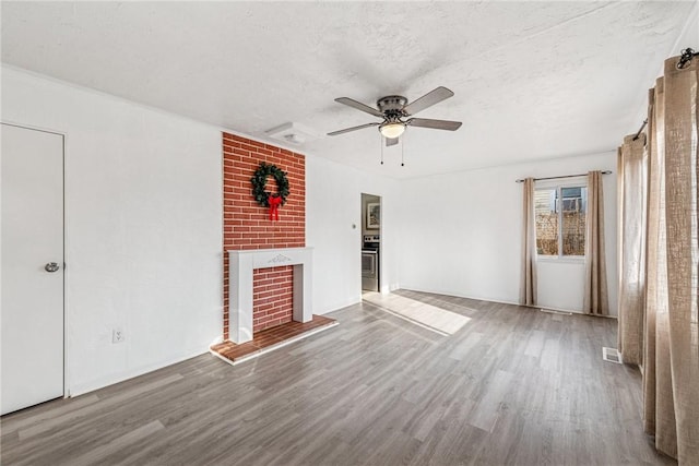 unfurnished living room with a textured ceiling, a fireplace, wood finished floors, and visible vents