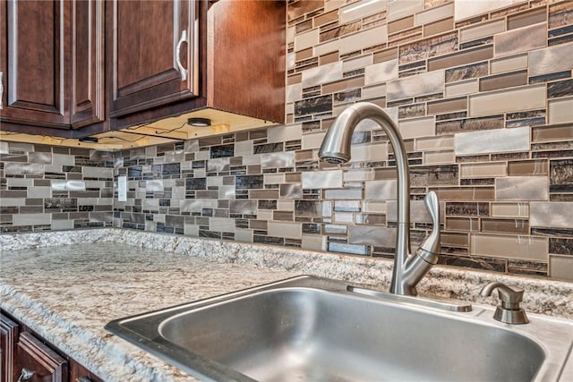 details featuring tasteful backsplash, light stone counters, dark brown cabinets, and a sink