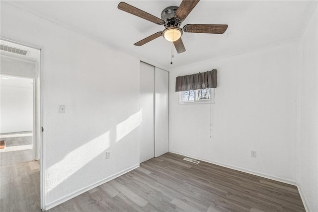 empty room with ceiling fan, wood finished floors, visible vents, and baseboards