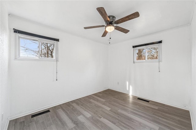 empty room with ceiling fan, wood finished floors, visible vents, and baseboards