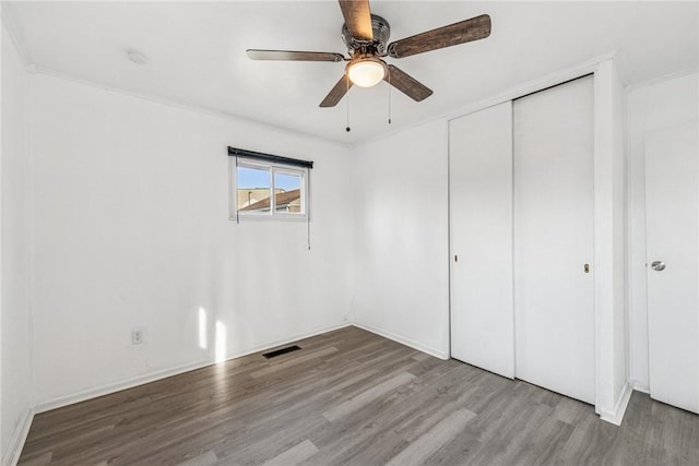 unfurnished bedroom featuring crown molding, a closet, visible vents, ceiling fan, and wood finished floors