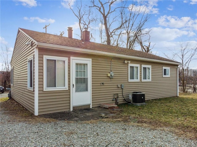 rear view of house featuring a shingled roof, central AC, and a chimney