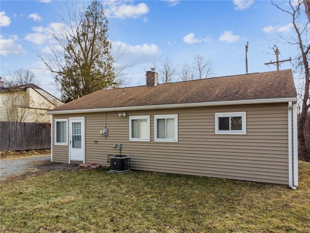 back of property with a chimney, a shingled roof, a lawn, central AC, and fence