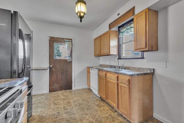 kitchen with brown cabinets, dark countertops, appliances with stainless steel finishes, a sink, and baseboards