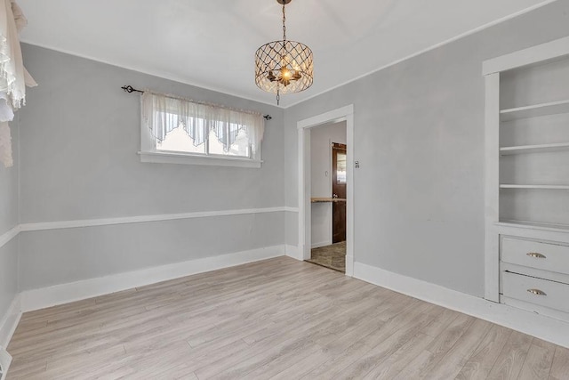 unfurnished room featuring baseboards, a chandelier, and wood finished floors