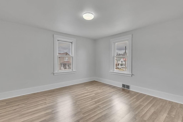 unfurnished room with light wood-type flooring, visible vents, and baseboards