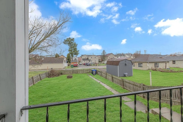 view of yard featuring a residential view, a fenced backyard, an outdoor structure, and a storage unit