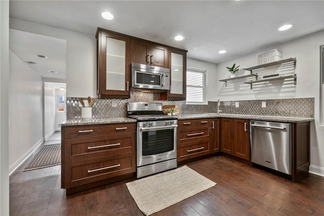 kitchen featuring appliances with stainless steel finishes, dark wood-type flooring, backsplash, and light stone counters